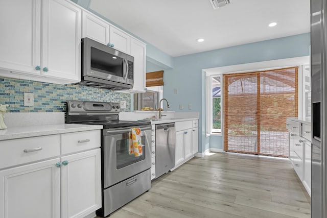 kitchen featuring sink, stainless steel appliances, light hardwood / wood-style floors, decorative backsplash, and white cabinets