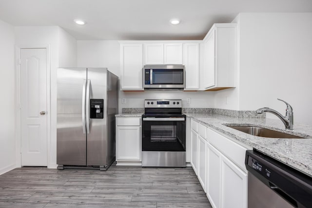 kitchen with sink, light hardwood / wood-style flooring, appliances with stainless steel finishes, light stone counters, and white cabinets