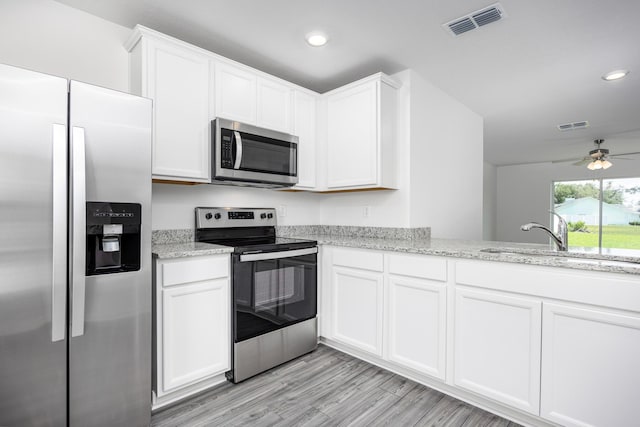 kitchen featuring sink, white cabinetry, stainless steel appliances, light stone counters, and light hardwood / wood-style floors