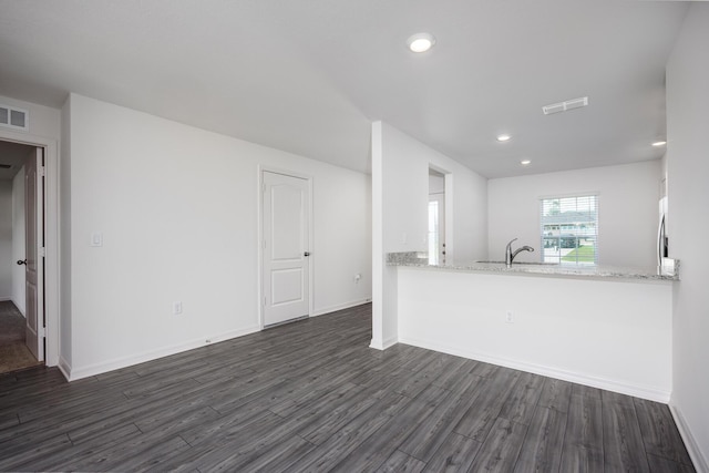 kitchen with light stone counters, dark hardwood / wood-style flooring, kitchen peninsula, and sink