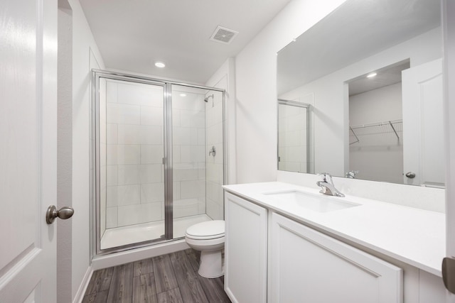 bathroom featuring wood-type flooring, toilet, a shower with shower door, and vanity