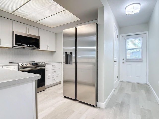 kitchen with stainless steel appliances, baseboards, white cabinets, light wood-type flooring, and tasteful backsplash