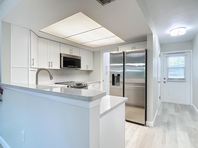 kitchen with light wood finished floors, appliances with stainless steel finishes, a peninsula, light countertops, and white cabinetry