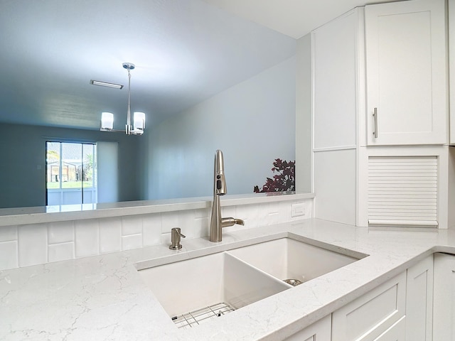 kitchen with a chandelier, light stone counters, a sink, white cabinets, and pendant lighting