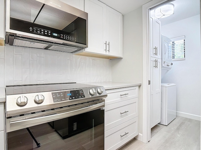 kitchen featuring light countertops, backsplash, appliances with stainless steel finishes, white cabinetry, and stacked washing maching and dryer