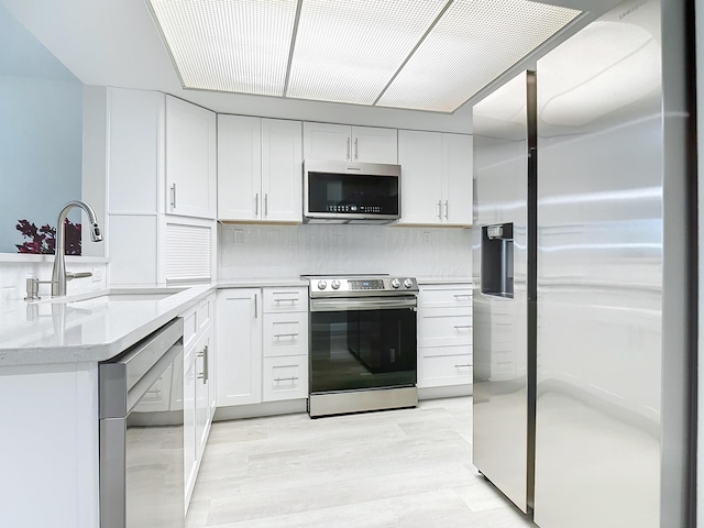 kitchen featuring white cabinets, light stone countertops, stainless steel appliances, light wood-style floors, and a sink