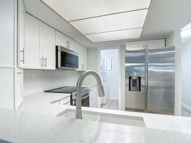 kitchen with light stone counters, a sink, white cabinets, appliances with stainless steel finishes, and backsplash