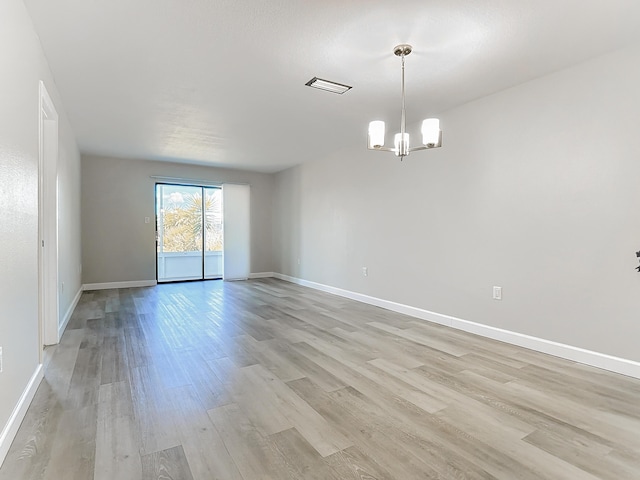 spare room with baseboards, light wood-type flooring, visible vents, and an inviting chandelier