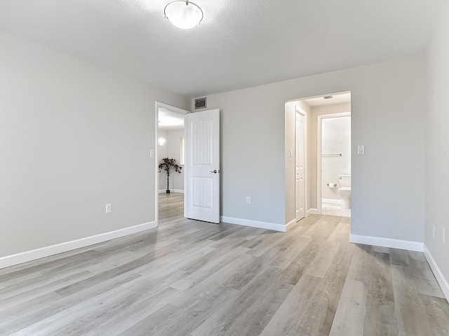 unfurnished bedroom featuring a textured ceiling, light wood-type flooring, visible vents, and baseboards