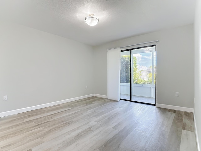 spare room featuring a textured ceiling, light wood-type flooring, and baseboards