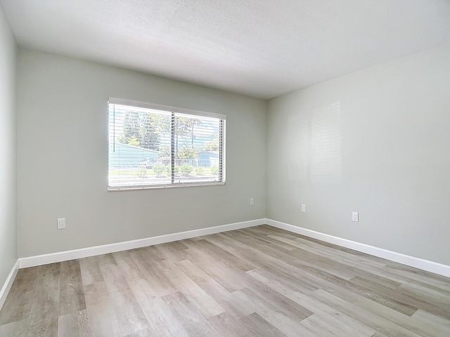 empty room featuring light wood-style floors, a textured ceiling, and baseboards