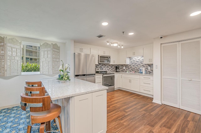 kitchen featuring dark wood-style floors, a peninsula, white cabinets, appliances with stainless steel finishes, and tasteful backsplash