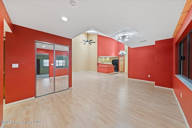 unfurnished living room with ceiling fan with notable chandelier, light wood-type flooring, a textured ceiling, and vaulted ceiling