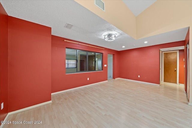 empty room featuring a textured ceiling, wood finished floors, visible vents, and baseboards