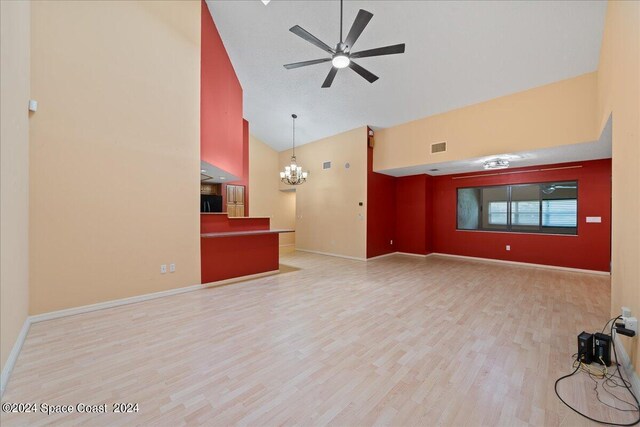 unfurnished living room with ceiling fan with notable chandelier, light wood-type flooring, and high vaulted ceiling