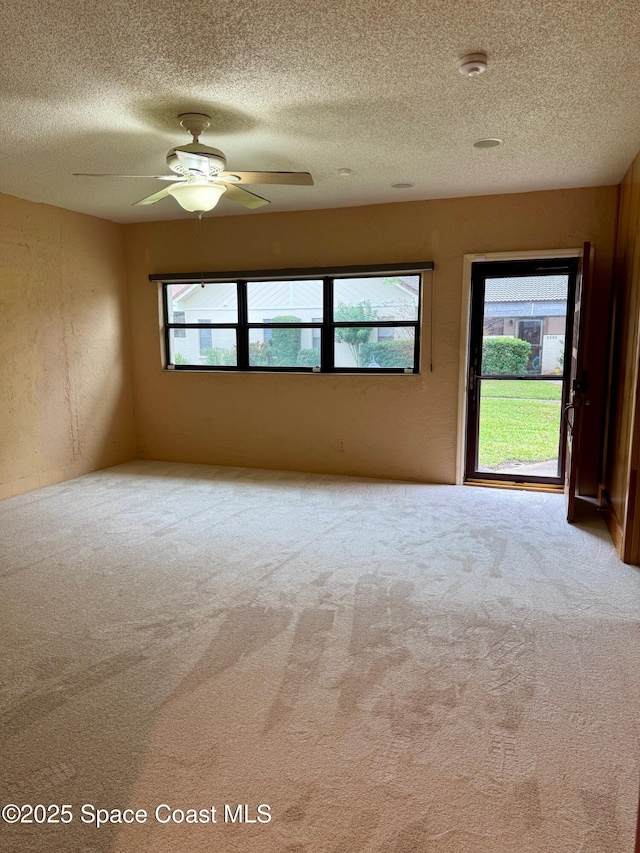 empty room with a textured ceiling, ceiling fan, light carpet, and a wealth of natural light