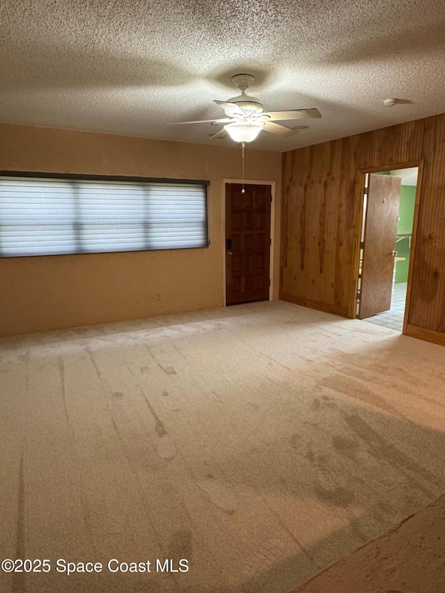 spare room featuring carpet, ceiling fan, a textured ceiling, and wooden walls