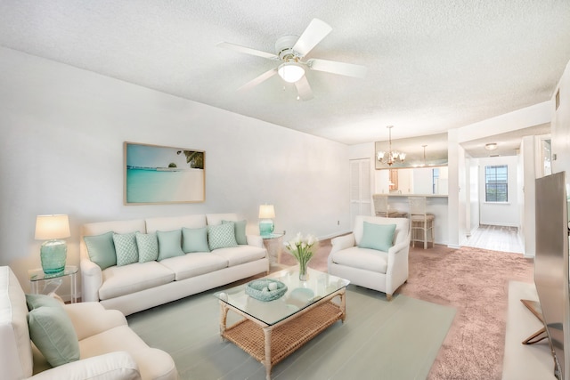 carpeted living room featuring a textured ceiling and ceiling fan with notable chandelier