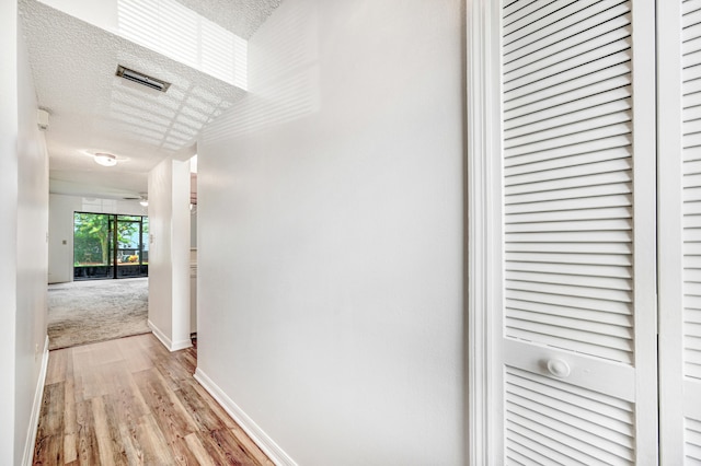 hallway featuring light hardwood / wood-style flooring and a textured ceiling