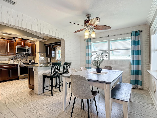 dining area featuring a textured ceiling, light hardwood / wood-style floors, ceiling fan, and brick wall