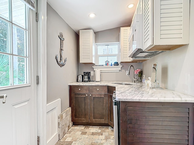 kitchen with sink, dark brown cabinets, light stone countertops, and a healthy amount of sunlight