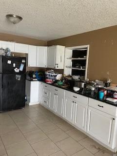 kitchen with white cabinets, black fridge, light tile patterned floors, and a textured ceiling