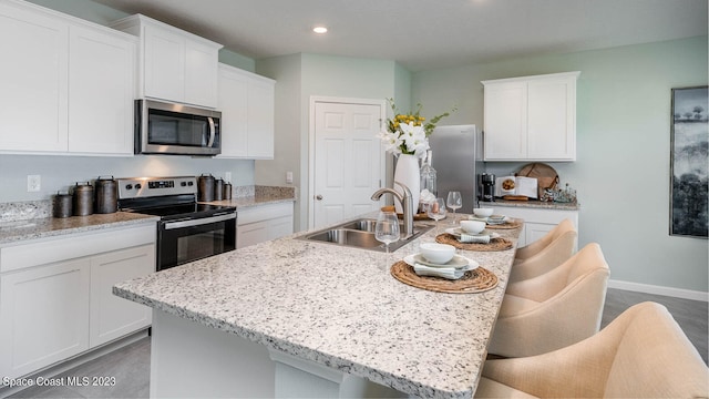 kitchen featuring sink, a kitchen island with sink, a kitchen breakfast bar, stainless steel appliances, and white cabinets