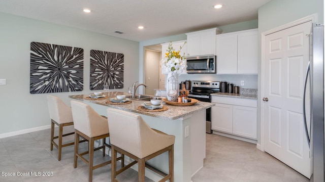 kitchen featuring sink, white cabinets, stainless steel appliances, and an island with sink