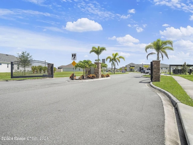 view of road featuring sidewalks, curbs, a gate, a residential view, and traffic signs