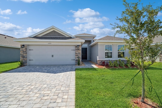 view of front of property featuring decorative driveway, stucco siding, an attached garage, a front yard, and stone siding