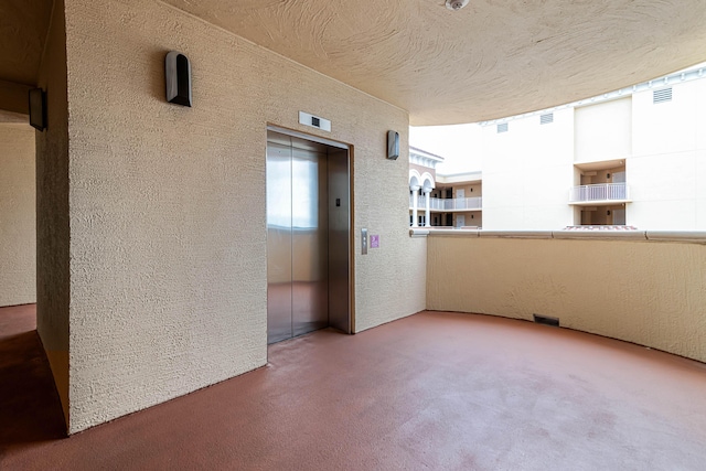 empty room featuring carpet, elevator, a textured wall, and a textured ceiling