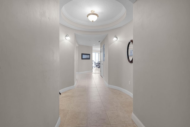 corridor featuring light tile patterned floors, a tray ceiling, and baseboards