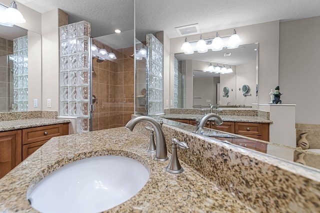 bathroom with tiled shower, vanity, and a textured ceiling