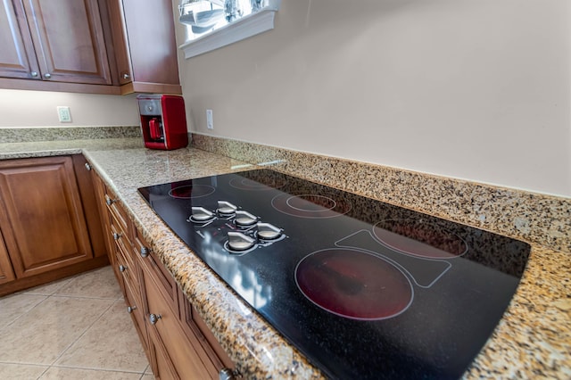 kitchen with black electric stovetop, light stone counters, and light tile patterned floors