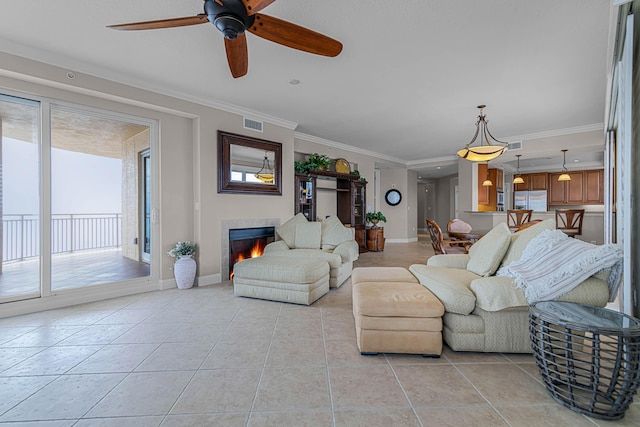 living room featuring ceiling fan, ornamental molding, a tile fireplace, and light tile patterned floors