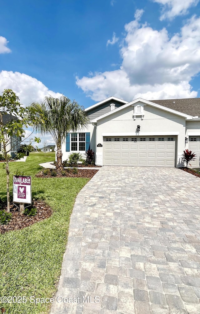 view of front facade with a front yard, decorative driveway, an attached garage, and stucco siding