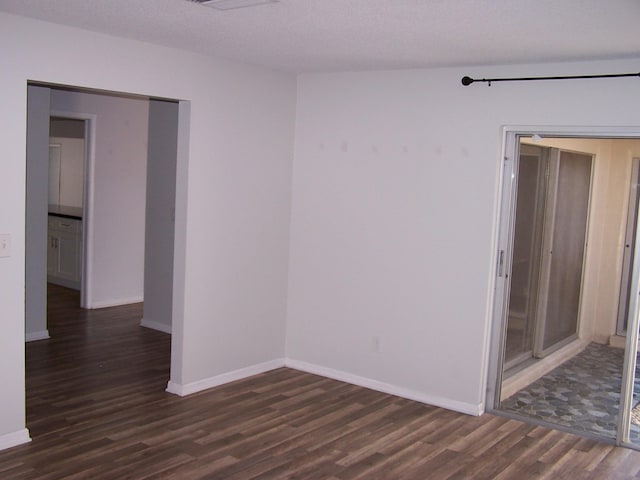 spare room with a textured ceiling, dark wood finished floors, and baseboards