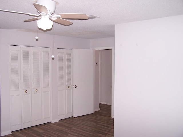 unfurnished bedroom featuring multiple closets, ceiling fan, a textured ceiling, and wood finished floors