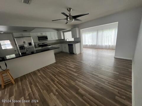 kitchen with ceiling fan, stainless steel appliances, white cabinetry, dark countertops, and dark wood finished floors