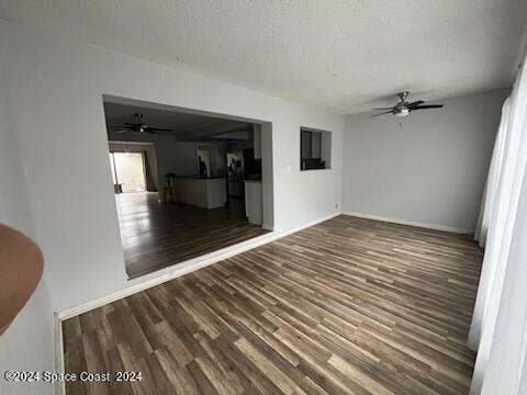 empty room featuring a textured ceiling, ceiling fan, wood finished floors, and baseboards