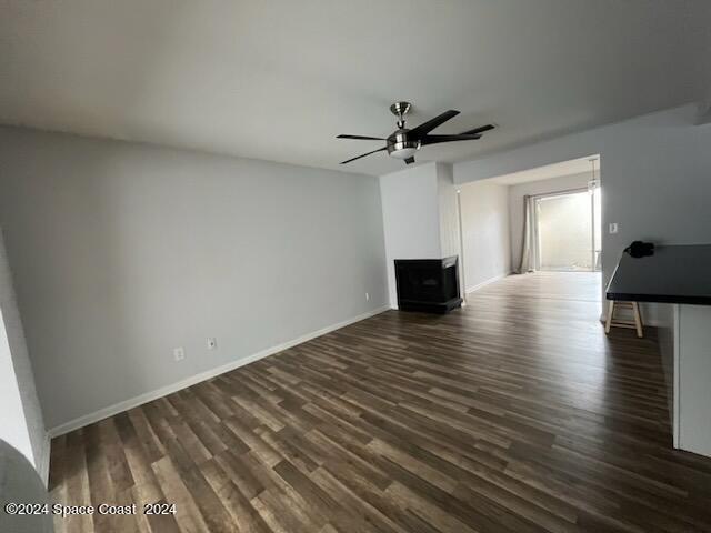 unfurnished living room with baseboards, a ceiling fan, and dark wood-type flooring