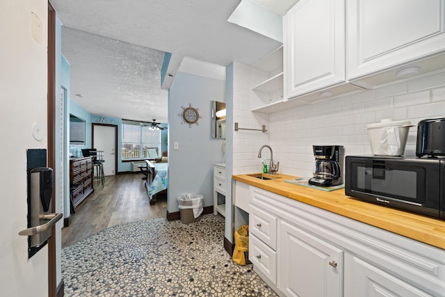 kitchen with sink, butcher block countertops, a textured ceiling, white cabinets, and backsplash