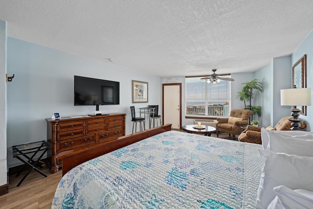 bedroom with ceiling fan, light hardwood / wood-style floors, and a textured ceiling