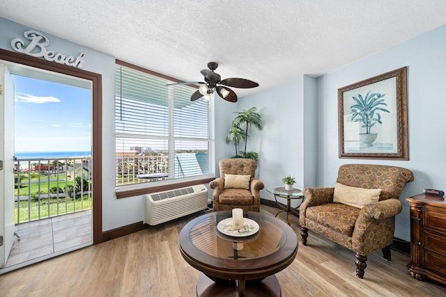 living area featuring a water view, a wall mounted AC, a textured ceiling, and light hardwood / wood-style flooring