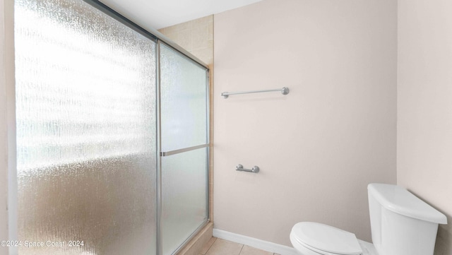 bathroom with tile patterned flooring, toilet, and a shower with door