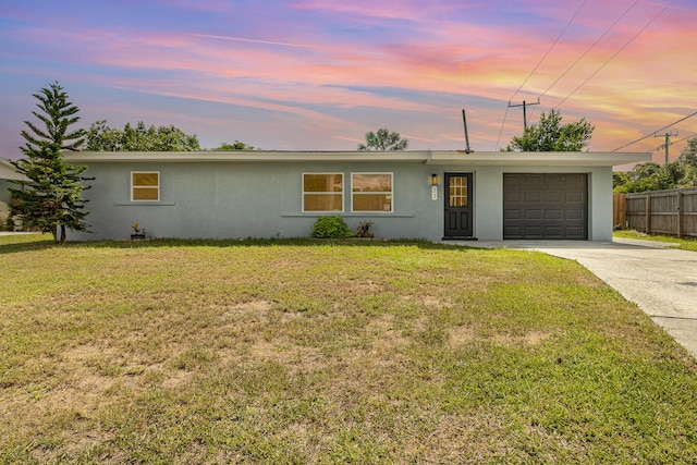 ranch-style house featuring an attached garage, fence, a yard, concrete driveway, and stucco siding