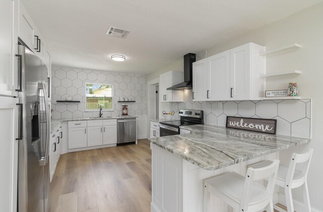 kitchen featuring decorative backsplash, white cabinetry, appliances with stainless steel finishes, and wall chimney exhaust hood