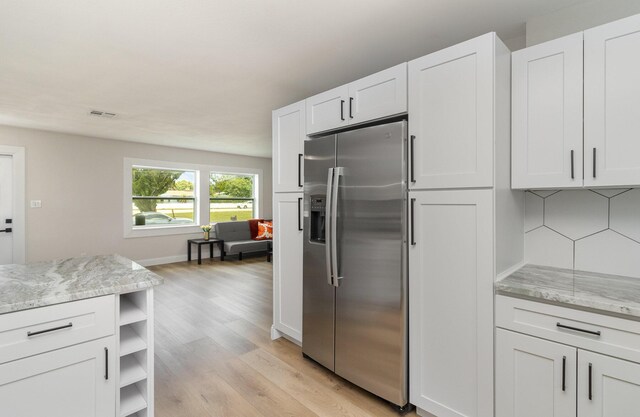 kitchen featuring tasteful backsplash, light stone counters, light hardwood / wood-style floors, stainless steel refrigerator with ice dispenser, and white cabinetry