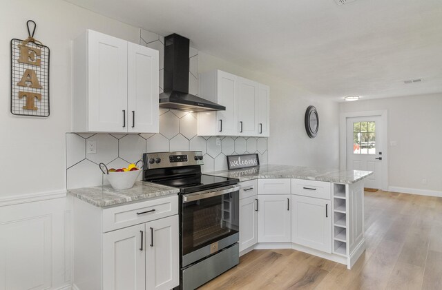 kitchen featuring stainless steel electric range oven, light hardwood / wood-style flooring, light stone counters, and wall chimney range hood