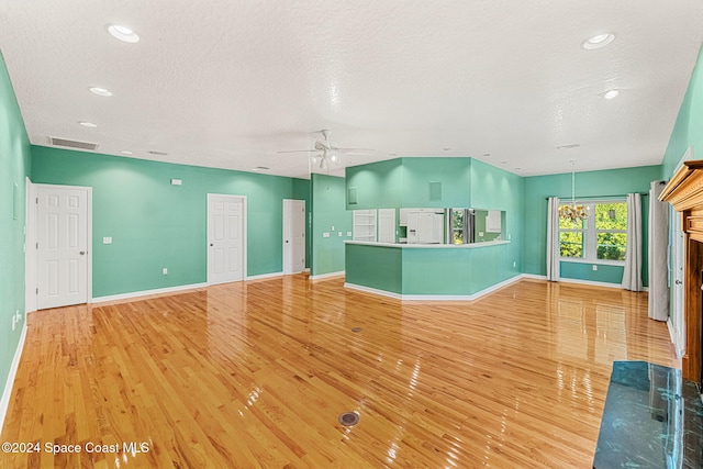 unfurnished living room with ceiling fan with notable chandelier, a textured ceiling, and light wood-type flooring